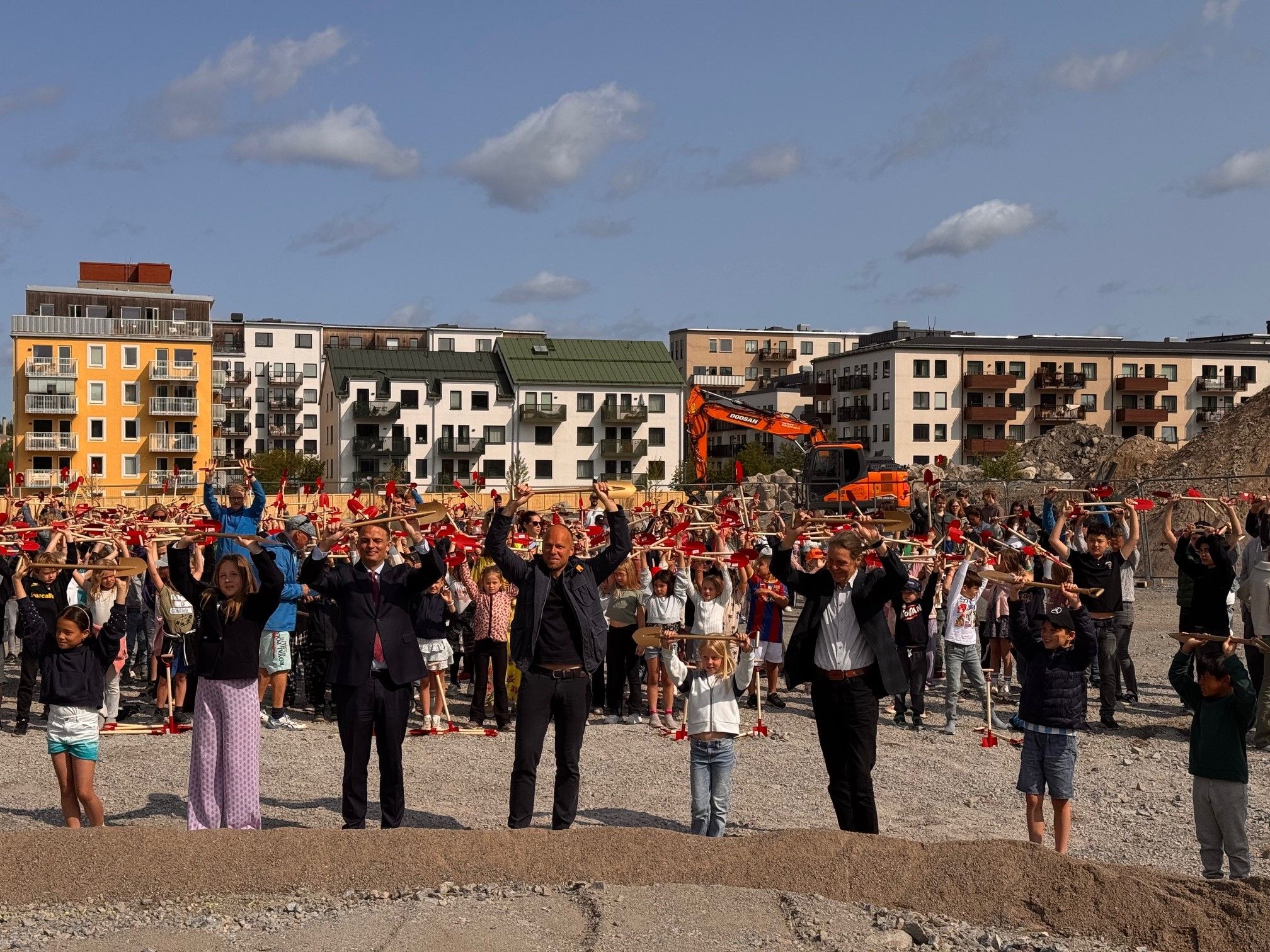 Politiker och elever höjer spadarna över huvudet vid tillfället för första spadtaget av nya Täby Parkskolan